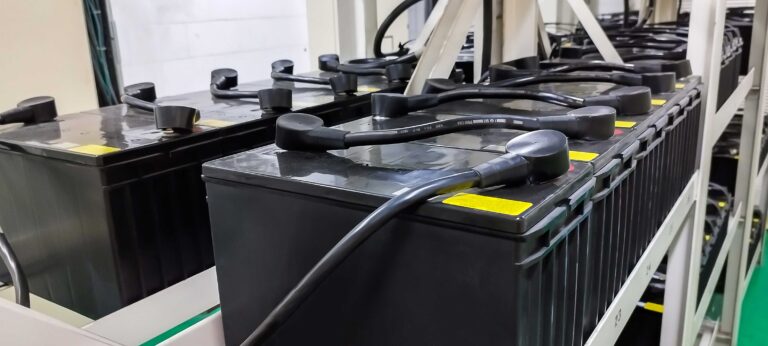 Large industrial UPS battery backup units lined up on metal racks, indicating when system maintenance or replacement is required.
